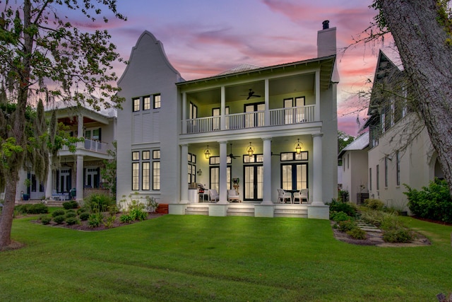 back house at dusk with ceiling fan, a balcony, central AC unit, and a lawn