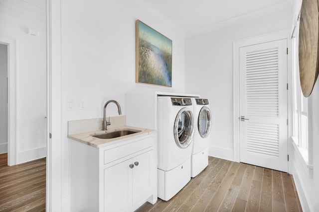 clothes washing area featuring sink, hardwood / wood-style flooring, cabinets, and washer and clothes dryer