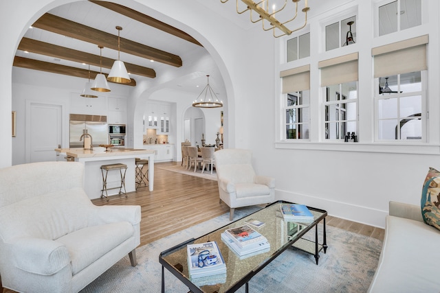 living room with sink, light hardwood / wood-style flooring, beam ceiling, and an inviting chandelier