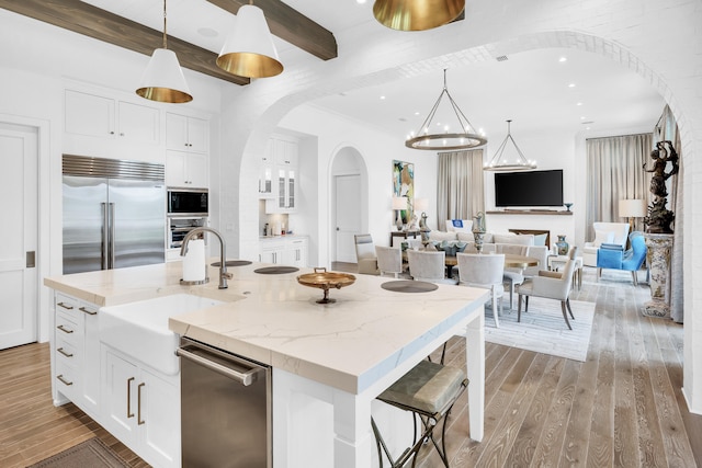 kitchen featuring pendant lighting, light hardwood / wood-style floors, white cabinetry, a kitchen island with sink, and built in appliances