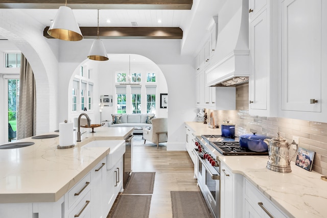 kitchen featuring appliances with stainless steel finishes, custom exhaust hood, light wood-type flooring, white cabinetry, and hanging light fixtures