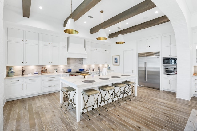 kitchen with beam ceiling, stainless steel built in fridge, custom exhaust hood, and decorative light fixtures