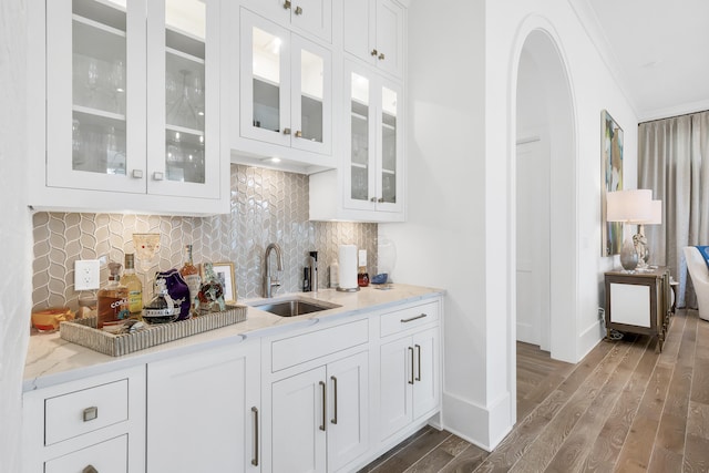 kitchen featuring wood-type flooring, crown molding, white cabinetry, sink, and tasteful backsplash