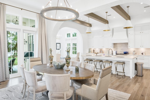 dining space featuring sink, beam ceiling, light wood-type flooring, and a chandelier