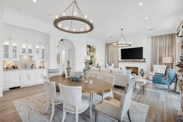 dining area with ornamental molding, an inviting chandelier, sink, and light wood-type flooring