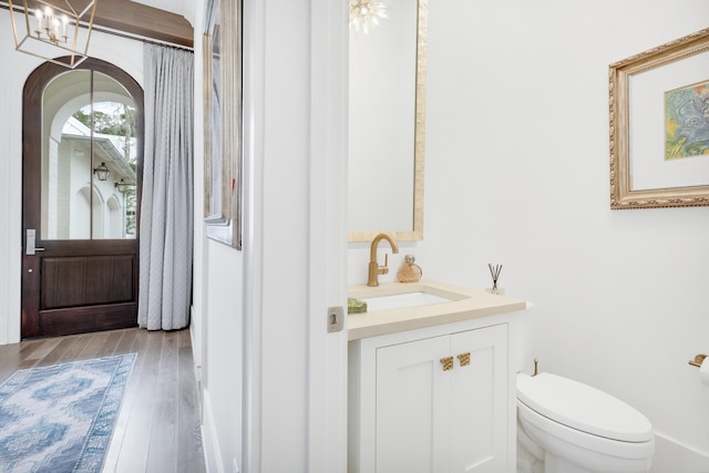 bathroom with hardwood / wood-style floors, vanity, an inviting chandelier, and toilet