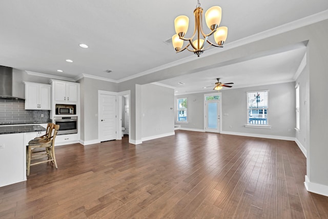 unfurnished living room with ceiling fan with notable chandelier, ornamental molding, and dark wood-type flooring