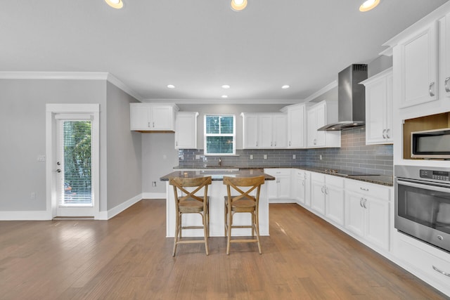 kitchen with wall chimney exhaust hood, tasteful backsplash, appliances with stainless steel finishes, and white cabinets