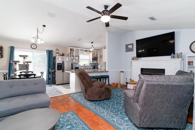 living room featuring lofted ceiling, light parquet floors, ceiling fan with notable chandelier, and a fireplace