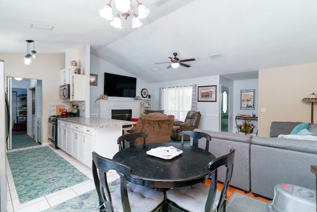 tiled dining space featuring ceiling fan with notable chandelier, vaulted ceiling, and a fireplace