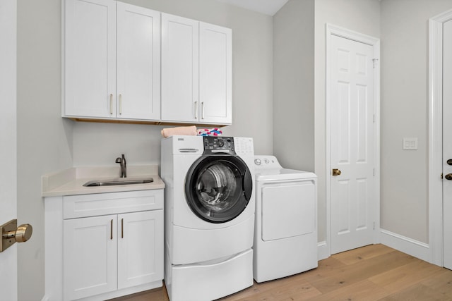 laundry room with light hardwood / wood-style flooring, sink, washing machine and dryer, and cabinets