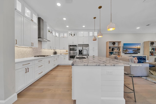 kitchen with light hardwood / wood-style flooring, wall chimney range hood, white cabinetry, and an island with sink