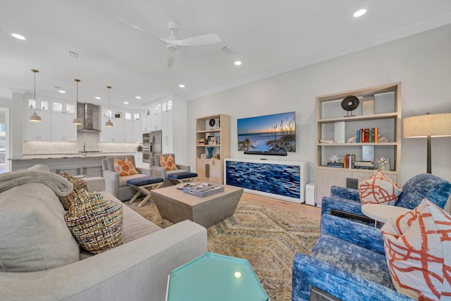 living room featuring wood-type flooring, ceiling fan, crown molding, and sink