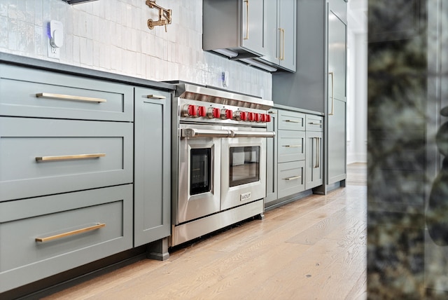 kitchen with backsplash, gray cabinets, light hardwood / wood-style floors, and range with two ovens