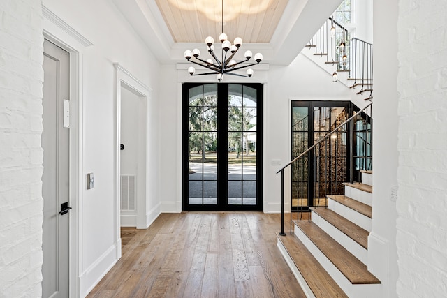 entryway with wood-type flooring, a tray ceiling, a notable chandelier, and french doors