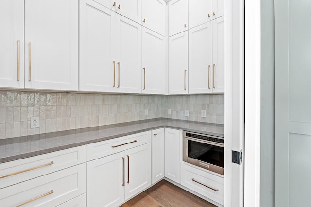 kitchen with dark hardwood / wood-style flooring, white cabinetry, backsplash, and stainless steel oven