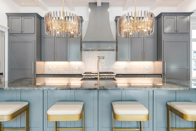 kitchen with an inviting chandelier, a kitchen bar, custom exhaust hood, and dark stone counters