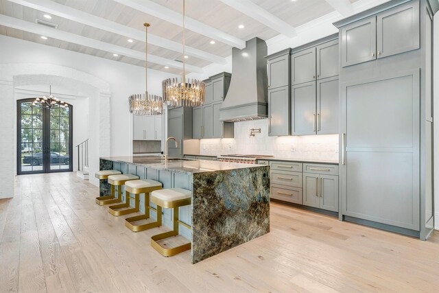 kitchen with dark stone counters, backsplash, custom range hood, light hardwood / wood-style floors, and beamed ceiling