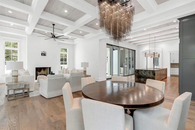 dining space with sink, ceiling fan with notable chandelier, light hardwood / wood-style flooring, and a large fireplace