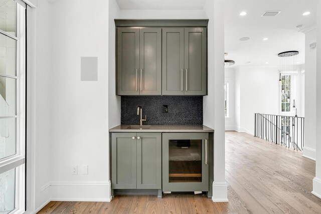 bar featuring sink, light hardwood / wood-style flooring, wine cooler, and backsplash