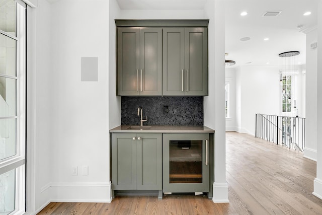 bar featuring sink, beverage cooler, backsplash, and light wood-type flooring