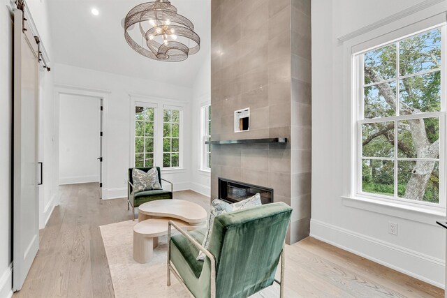 living area with a notable chandelier, light hardwood / wood-style floors, a tiled fireplace, and a barn door