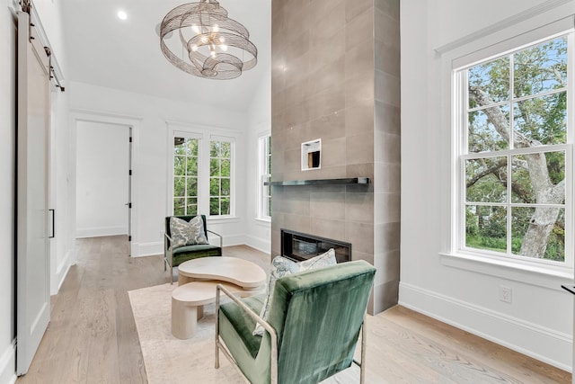 living room featuring a tiled fireplace, a barn door, plenty of natural light, and light hardwood / wood-style flooring