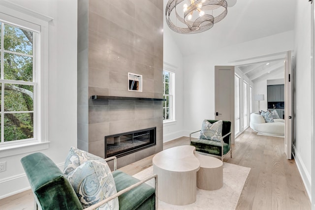 living room featuring light hardwood / wood-style flooring, a chandelier, a fireplace, lofted ceiling, and tile walls