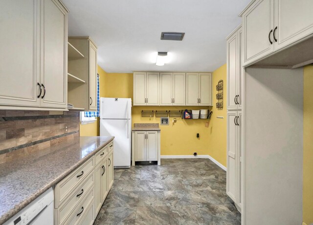 kitchen featuring white appliances, light stone countertops, backsplash, cream cabinetry, and dark tile flooring