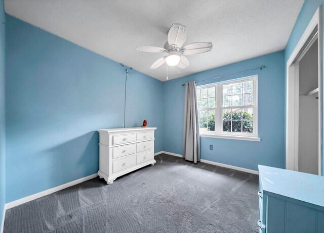 unfurnished bedroom with a textured ceiling, a closet, ceiling fan, and dark colored carpet