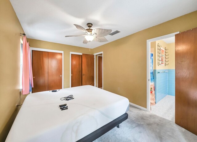 bedroom featuring light colored carpet, connected bathroom, ceiling fan, and two closets