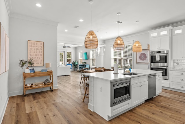 kitchen featuring a kitchen island with sink, ornamental molding, a sink, light wood-style floors, and appliances with stainless steel finishes