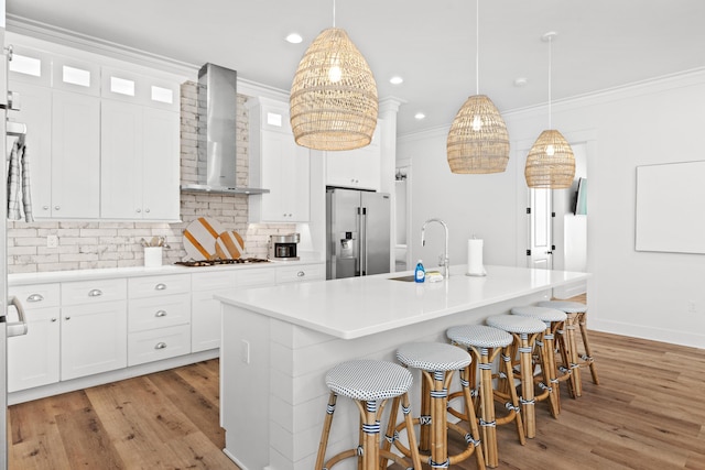 kitchen with a sink, high quality fridge, ornamental molding, and wall chimney range hood