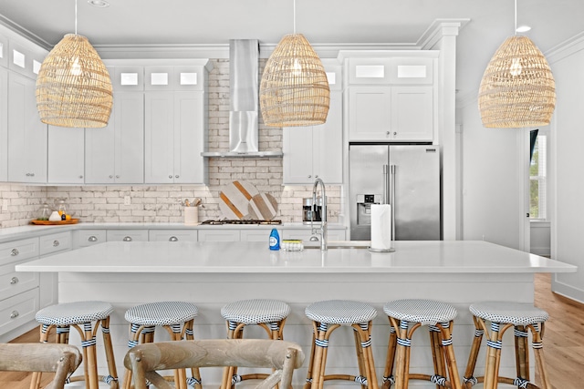 kitchen featuring decorative backsplash, high quality fridge, wall chimney exhaust hood, and ornamental molding