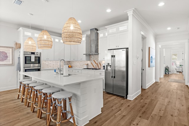 kitchen featuring visible vents, wall chimney range hood, ornamental molding, appliances with stainless steel finishes, and a sink