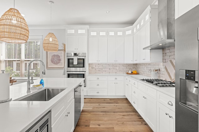 kitchen with a sink, stainless steel appliances, wall chimney exhaust hood, light wood finished floors, and light countertops