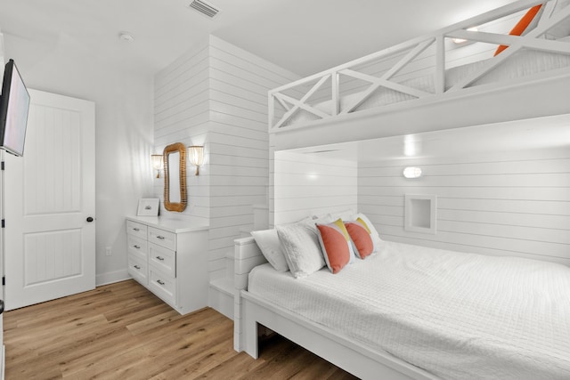 bedroom featuring light wood-type flooring, visible vents, and wooden walls