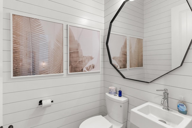 half bath with a sink, toilet, and wooden walls