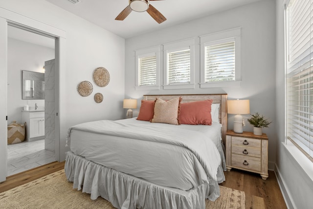 bedroom featuring a ceiling fan, wood finished floors, baseboards, a sink, and ensuite bathroom