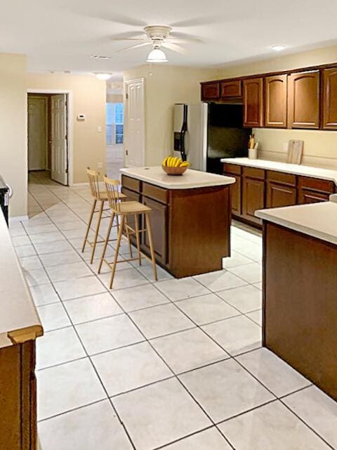 kitchen with a center island, stainless steel fridge, light tile patterned floors, ceiling fan, and a kitchen breakfast bar