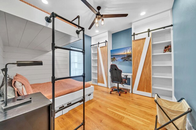 bedroom with light hardwood / wood-style flooring, ceiling fan, and a barn door