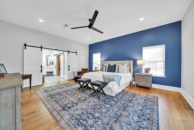 bedroom with a barn door, light hardwood / wood-style floors, and ceiling fan