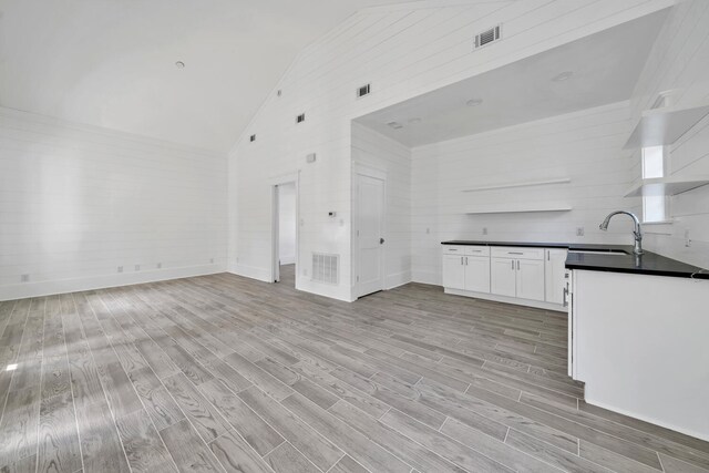 unfurnished living room featuring high vaulted ceiling, sink, and light hardwood / wood-style floors