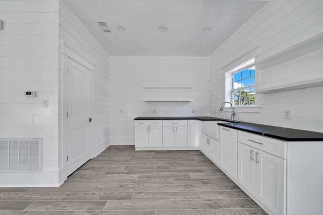 kitchen featuring wooden walls, light hardwood / wood-style flooring, white cabinets, and sink