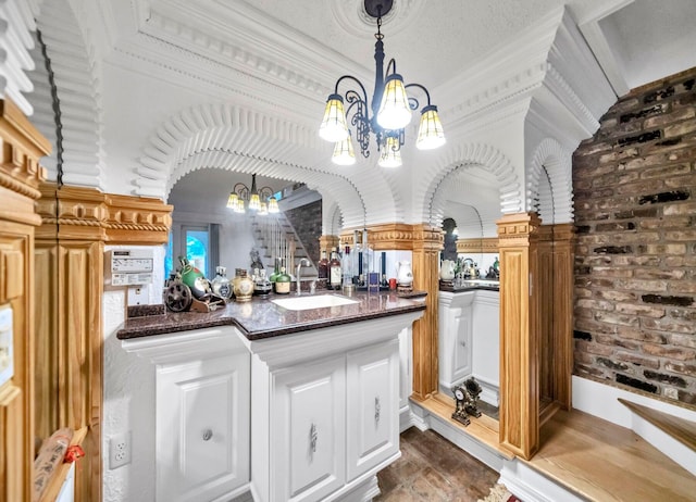 kitchen with a notable chandelier, sink, dark stone counters, decorative light fixtures, and brick wall