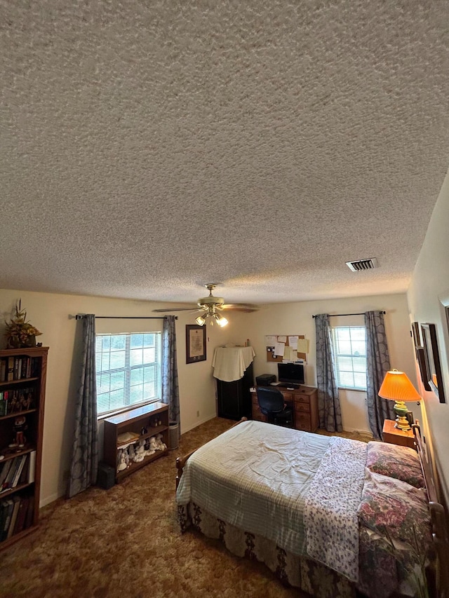 bedroom featuring a textured ceiling, ceiling fan, carpet, and multiple windows