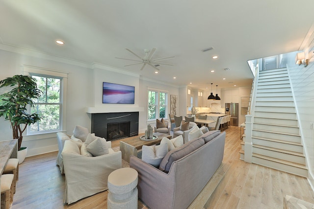 living room featuring ornamental molding, a healthy amount of sunlight, ceiling fan, and light wood-type flooring