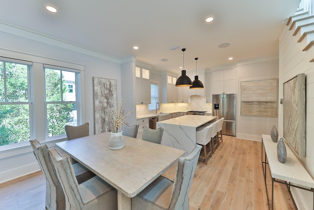 dining room with sink, crown molding, and light wood-type flooring