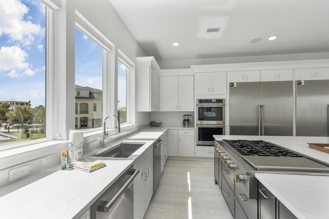 kitchen with light stone counters, white cabinets, sink, light hardwood / wood-style floors, and stainless steel appliances