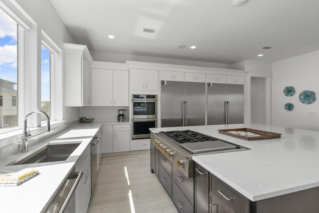 kitchen featuring light stone countertops, appliances with stainless steel finishes, light hardwood / wood-style flooring, white cabinets, and sink